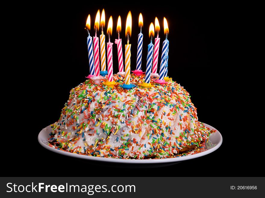 A cake with many coloured candles before black background. A cake with many coloured candles before black background