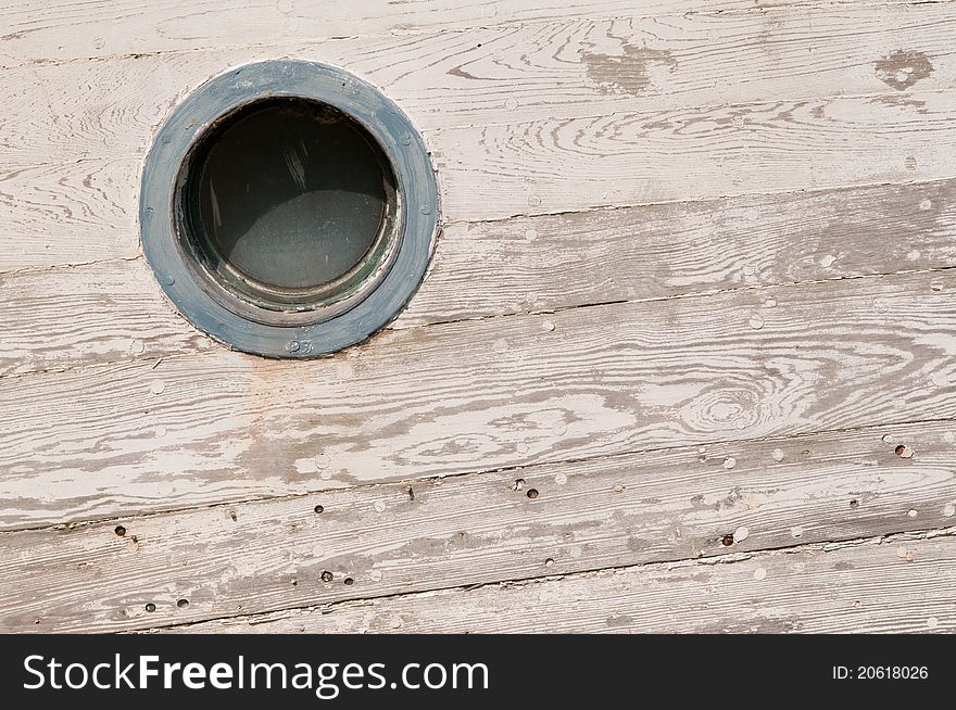 A shipwrecked wooden boat showwing a blue porthole with white faded paint. A shipwrecked wooden boat showwing a blue porthole with white faded paint.