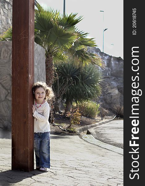 Cute small girl is laughing behind a column in front of the palm tree. Cute small girl is laughing behind a column in front of the palm tree