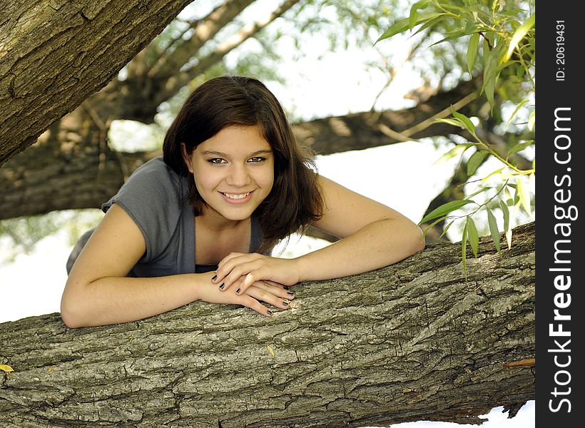 A beautiful young teen relaxed and smiling from between large tree branches. A beautiful young teen relaxed and smiling from between large tree branches.