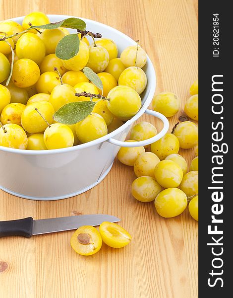 Studio-shot of small yellow plums also known as mellow mirabelles, on a wooden countertop. one is halved with a knife.