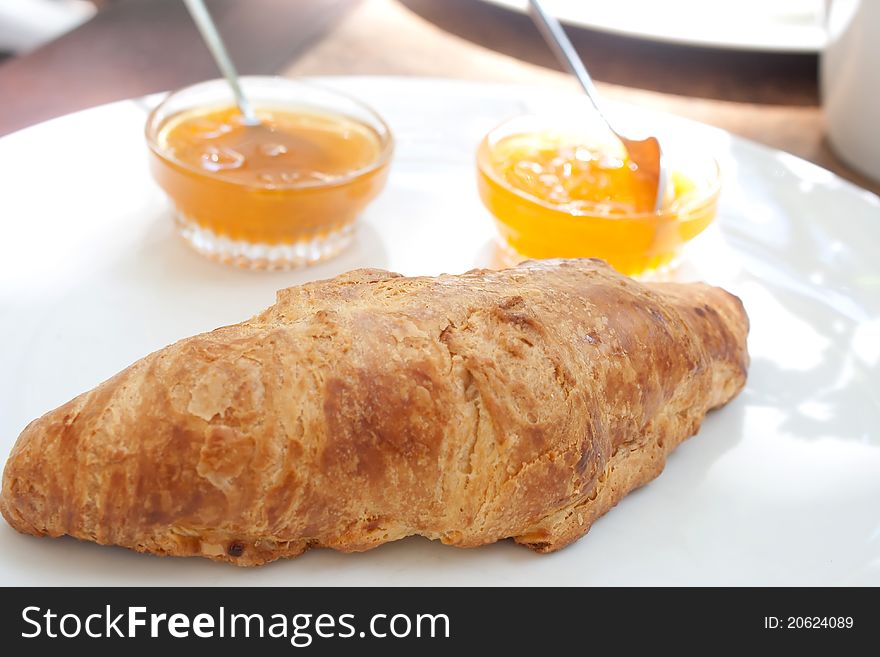 Large croissant on a plate with a portion of jam in a cafe shooting