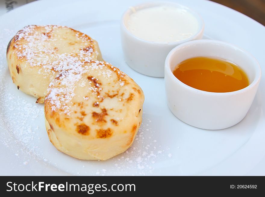Russian desert named syrniki (quark cheese pancakes) with sour cream and honey