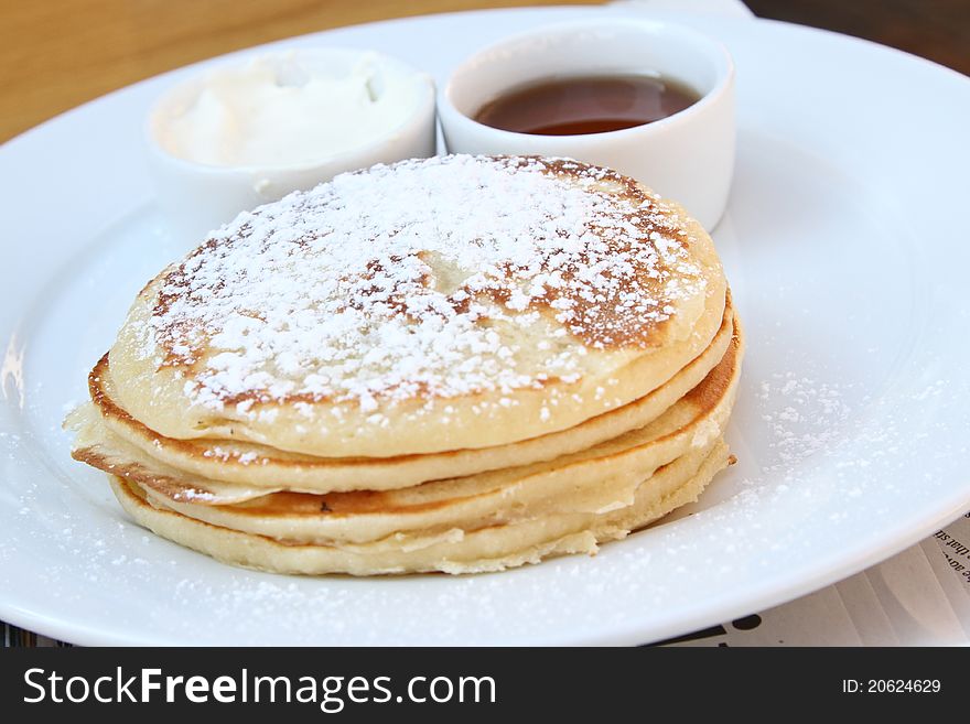 Pancakes on a white plate with sour cream and maple syrup