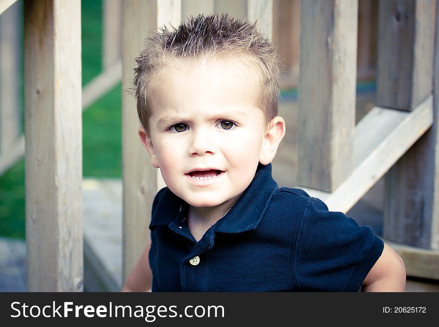 A cute brown eyed two year old boy in blue shirt sitting on wood stairs. A cute brown eyed two year old boy in blue shirt sitting on wood stairs