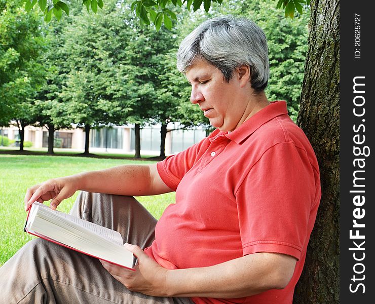 Middle-aged woman reading book by tree