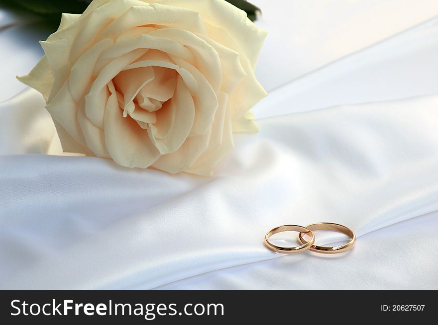 Wedding rings and a tea rose on white silk