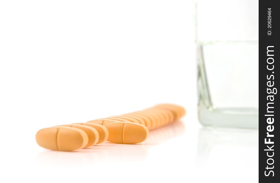 Vitamins lie in a row with glass of water on a white background