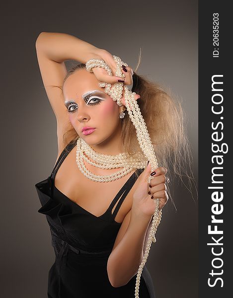 Beuatiful fair-haired professionally made-up girl wearing little black dress playing with pearl beads. Beuatiful fair-haired professionally made-up girl wearing little black dress playing with pearl beads