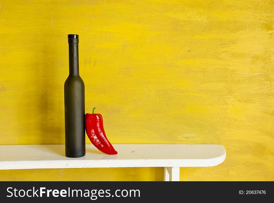 Black bottle and red pepper on yellow background