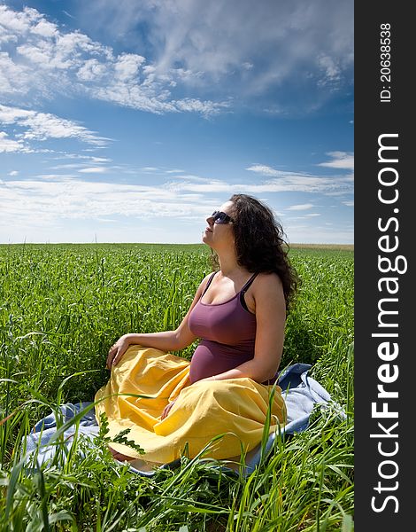 Pregnant woman on green grass field under blue sky in summer