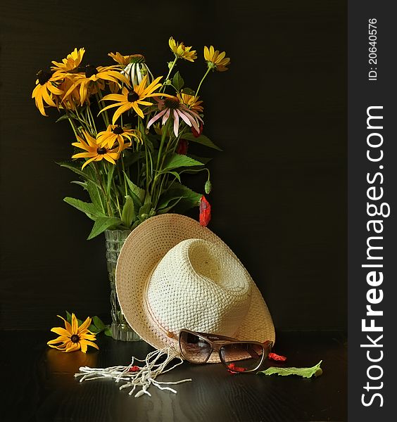 A vase of yellow wildflowers, hat and sunglasses