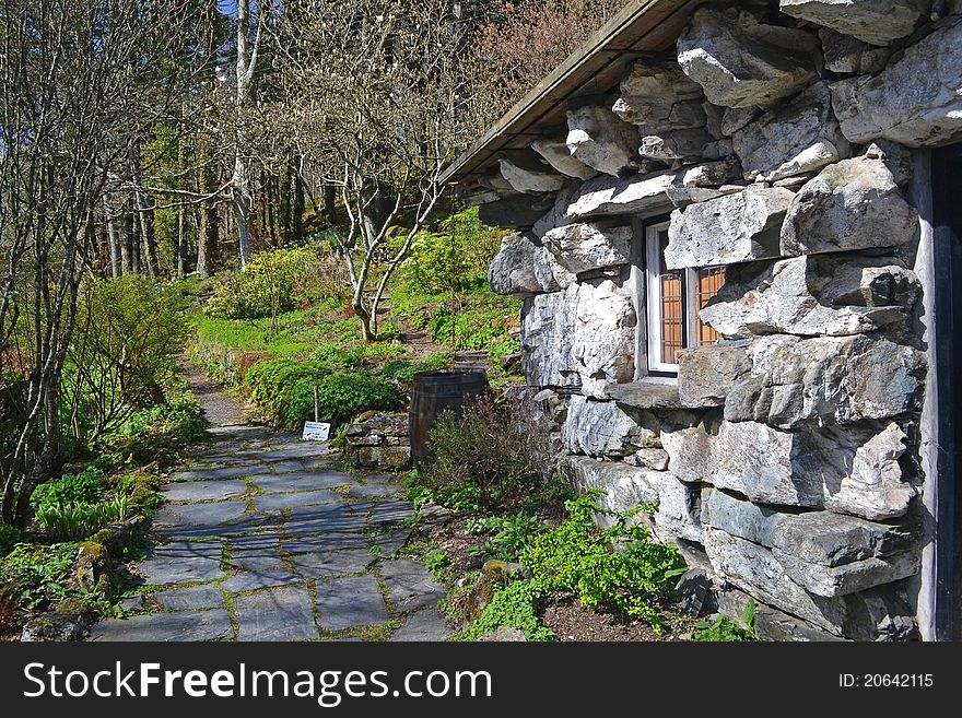 A stone house with crazy-paving leading to a path through the woods. A stone house with crazy-paving leading to a path through the woods