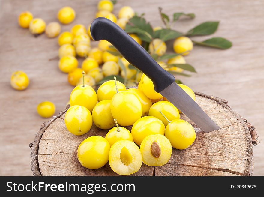 Studio-shot of small yellow plums also known as mellow mirabelles, on a tree trunk. one is halved with a knife.
