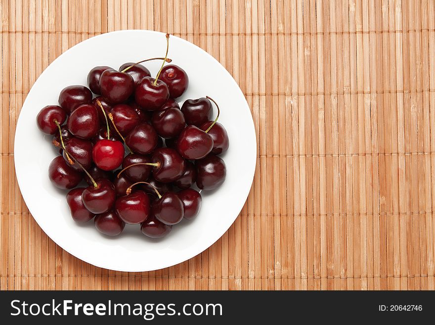 Sweet cherry on a white dish. Dish on a wooden cloth. Sweet cherry on a white dish. Dish on a wooden cloth.