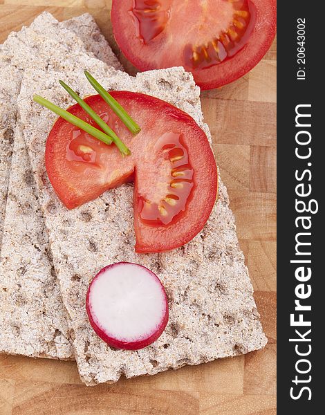 Studio-shot of a wooden board with crispbread, tomatoes,chives and radish. concept image for uncooked diet food