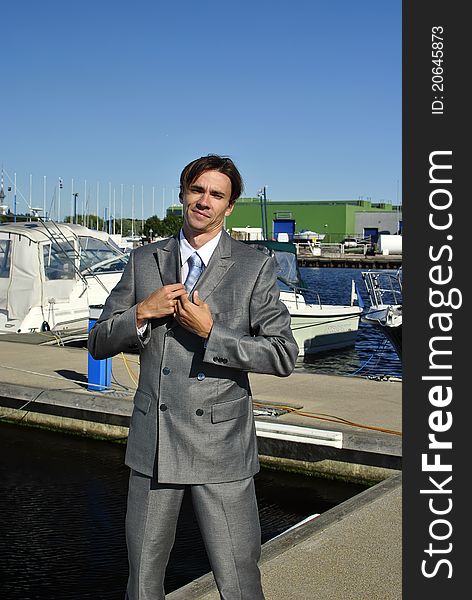 Man in a gray business suit straightens his tie, in the background of yachts