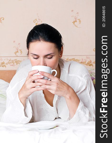 A young woman holding white a cup of coffee on bed at bedroom. A young woman holding white a cup of coffee on bed at bedroom