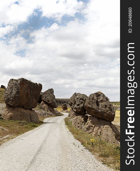 Precarious balanced volcanic rocks on either side of a public dirt track, Cappadocia, Turkey. Volcanic terrain, lava rock, limestone, sandstone, blue cloud layered sky, portrait, copy space, crop area, scenic