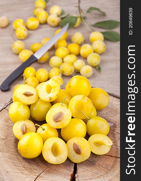 Studio-shot of small yellow plums also known as mellow mirabelles, on a tree trunk. some are halved with a knife.