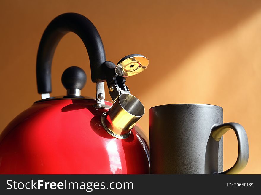 Closeup of red metal kettle near black mug on background with sunbeam. Closeup of red metal kettle near black mug on background with sunbeam