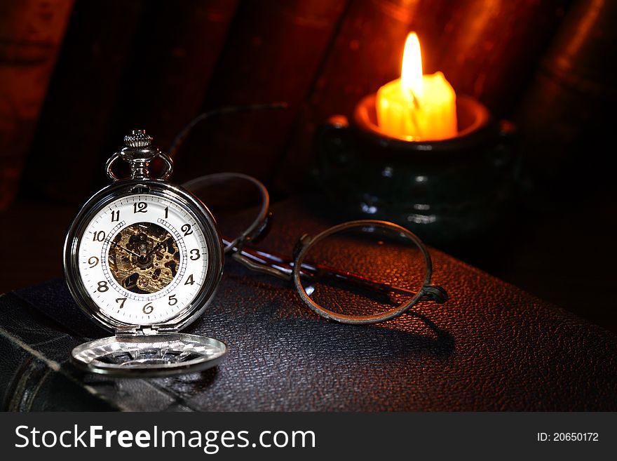 Vintage pocket watch near spectacles and candle on dark background. Vintage pocket watch near spectacles and candle on dark background