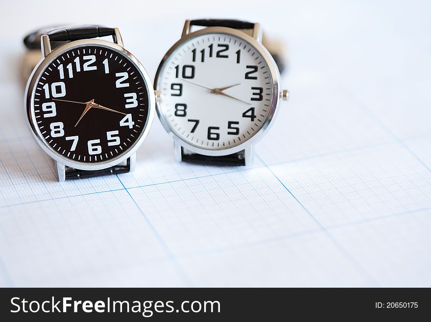 Pair of modern wristwatches standing on graph paper surface. Pair of modern wristwatches standing on graph paper surface