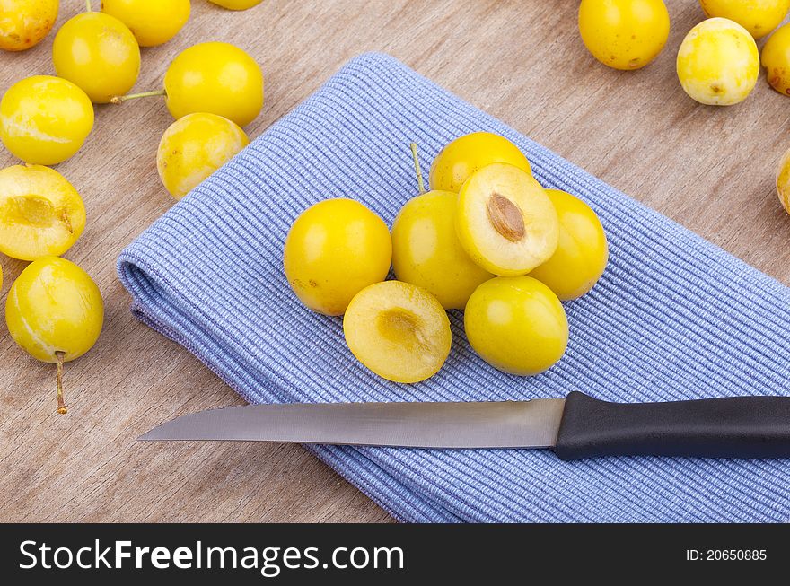 Studio-shot of small yellow plums also known as mellow mirabelles, on a table napkin. one is halved with a knife.