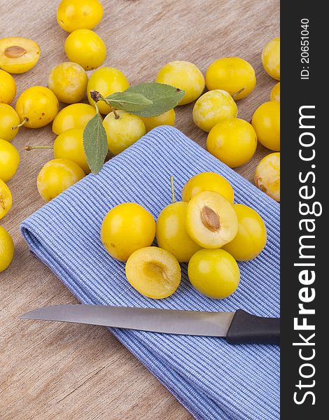 Studio-shot of small yellow plums also known as mellow mirabelles, on a table napkin. one is halved with a knife.