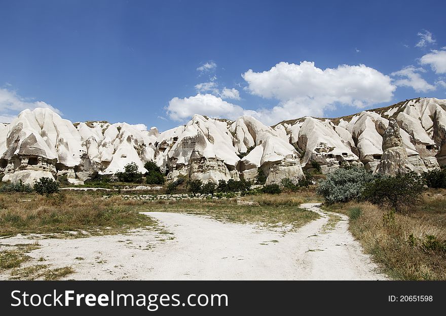 Landscape of mountainous terrain and cave houses serviced by dirt tracks, hinterlands, blue sky with cloud formation and wilderness surrounds, horizontal, copy space, crop area. Landscape of mountainous terrain and cave houses serviced by dirt tracks, hinterlands, blue sky with cloud formation and wilderness surrounds, horizontal, copy space, crop area