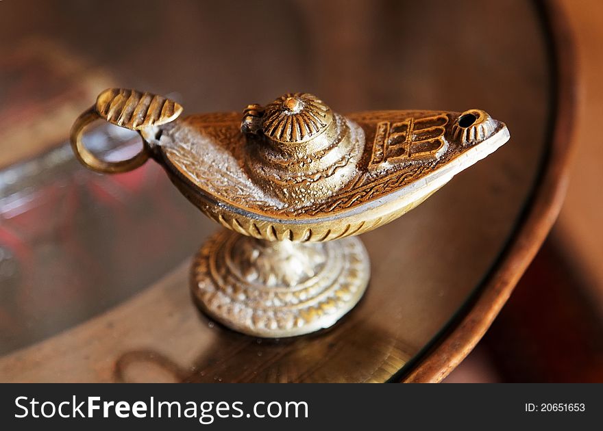 Ornate aladdin style genie lamp, brass lamp with handle on a round occasional table. Landscape, crop space and copy area. Ornate aladdin style genie lamp, brass lamp with handle on a round occasional table. Landscape, crop space and copy area.