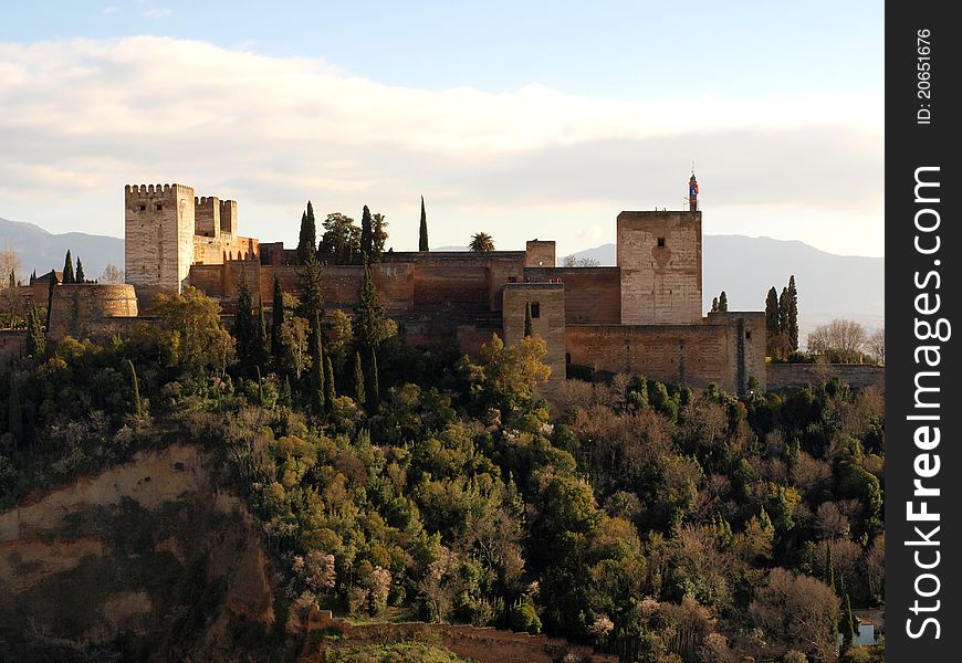 A view of the Alhambra palace fortress and towers with local vegetation on a hill. A view of the Alhambra palace fortress and towers with local vegetation on a hill.