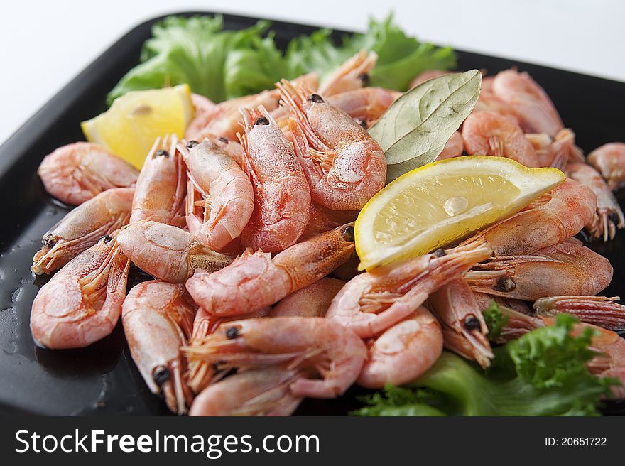 Coldwater shrimps with lettuce and lemon on the black plate