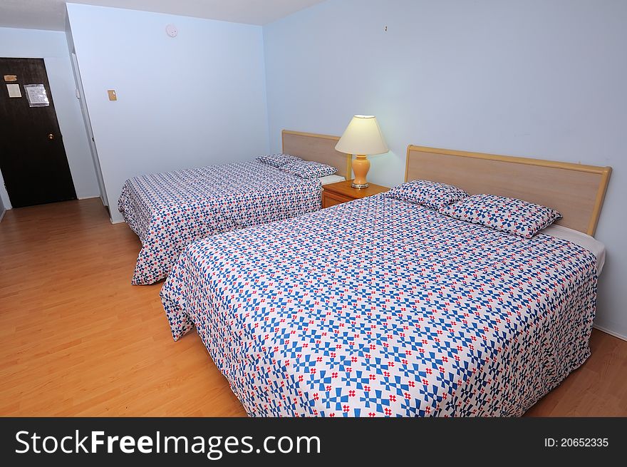 Large and simple room in hotel with double beds and wooden flooring.