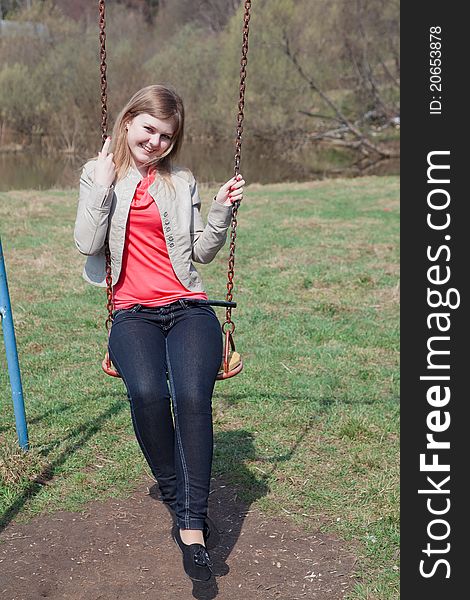 Young girl in the spring park sitting on the swing and smiling. Young girl in the spring park sitting on the swing and smiling