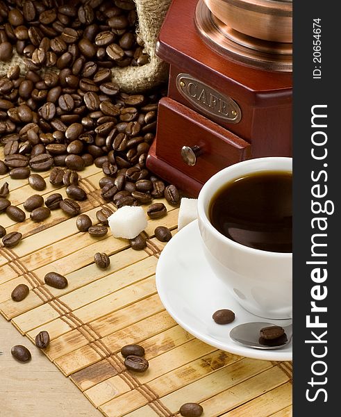 Cup of coffee and grinder with roasted beans on wooden background