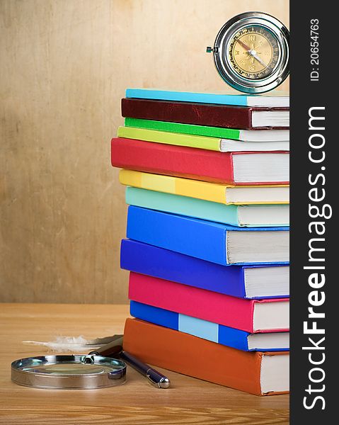 Pile of books, magnifier and compass with feather on wooden background