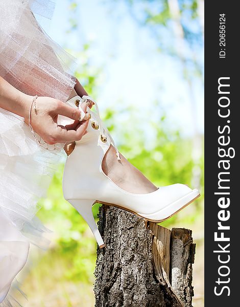 Bride lacing white shoes in the forest