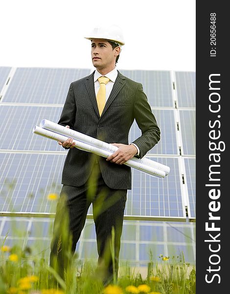 Male engineer at solar power station holding blueprints.