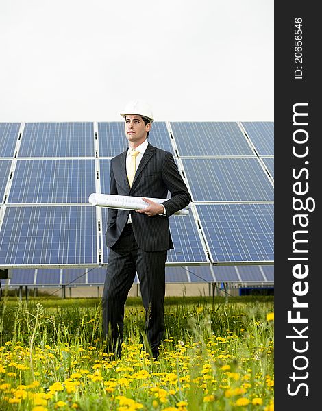 Male engineer at solar power station holding blueprints.