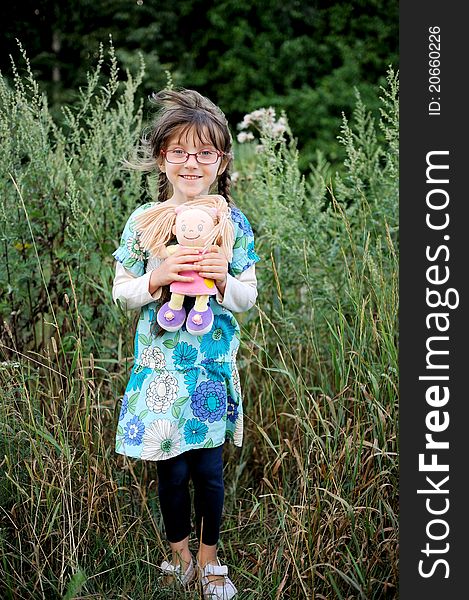 Adorable brunette child girl in glasses hugs her baby doll. Adorable brunette child girl in glasses hugs her baby doll