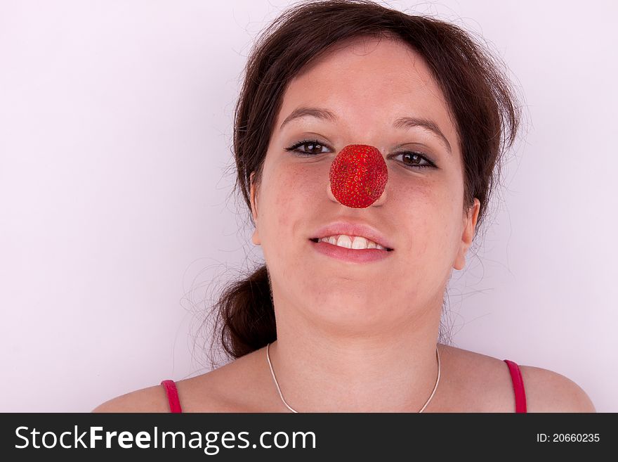 The pretty young woman has a strawberry on the nose. The pretty young woman has a strawberry on the nose