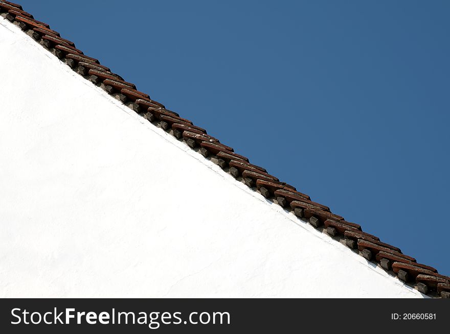 Brown roof tiles on a white building against a blue sky. Brown roof tiles on a white building against a blue sky