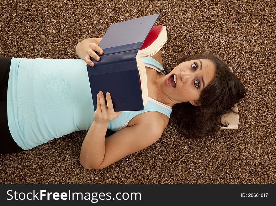 A woman with a shocked expression on her face while laying down reading a book. A woman with a shocked expression on her face while laying down reading a book.