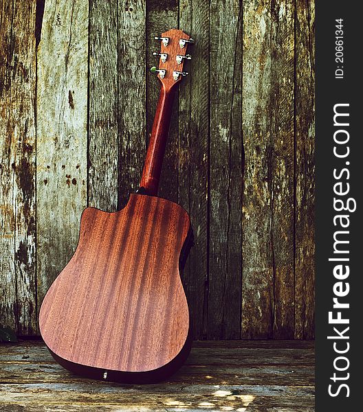 Richly toned back view of a classical guitar on a grunge wood backdrop with copy space. Richly toned back view of a classical guitar on a grunge wood backdrop with copy space.