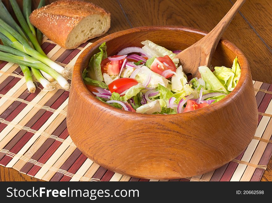 A bowl of tossed salad with green onions and crusty bread in the background