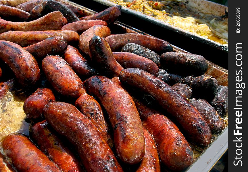 A bounty of juicy link sausages grilling over bbq at a festival on a sunny summer day. A bounty of juicy link sausages grilling over bbq at a festival on a sunny summer day.