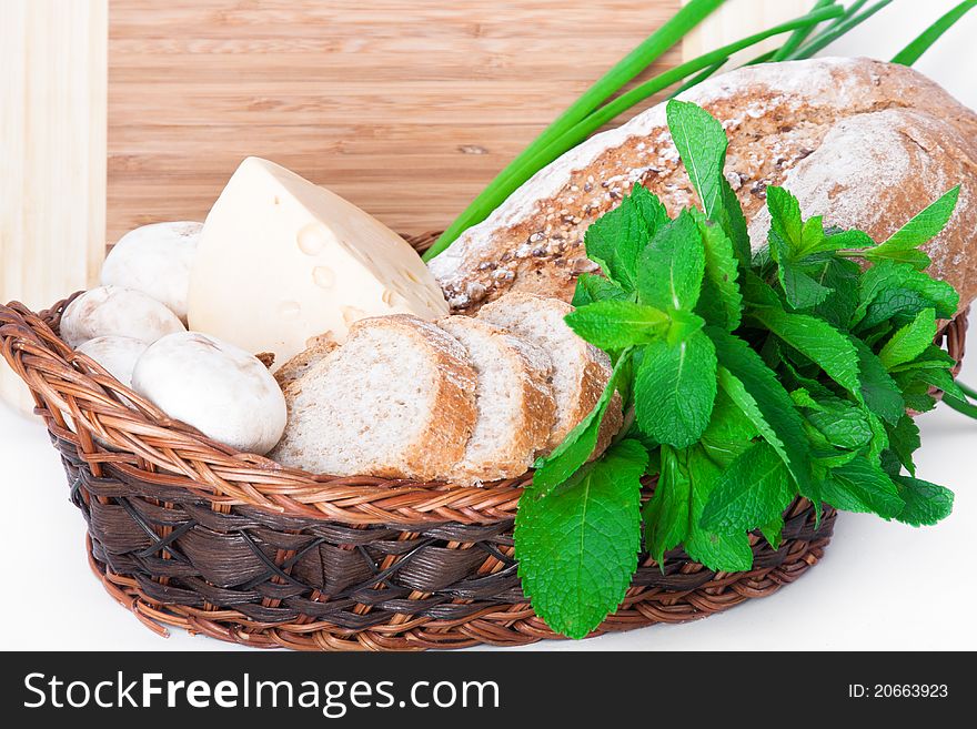The wooden basket with mushrooms, bread, cheese, mint, and green onions. The wooden basket with mushrooms, bread, cheese, mint, and green onions