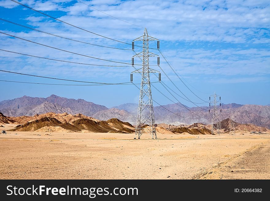 High voltage power electricity pylon line in the sand and the mountains