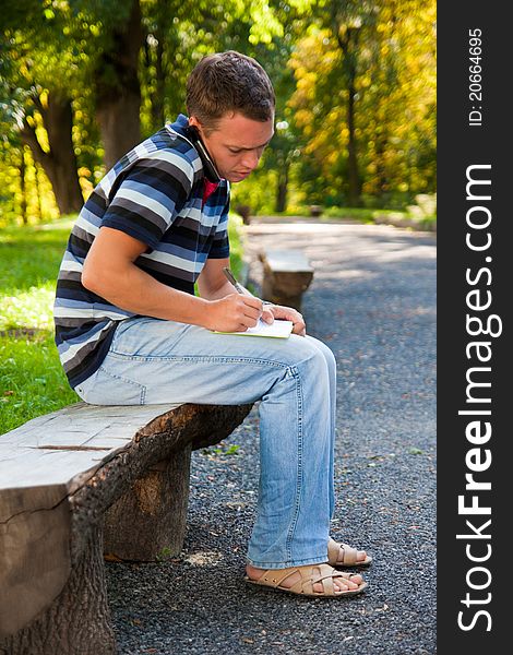 Man speaking on telephone and writing a note in the park. Man speaking on telephone and writing a note in the park